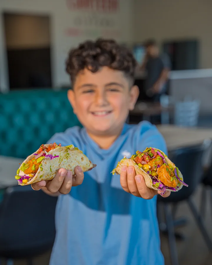 A kid holding two shrimp tacos