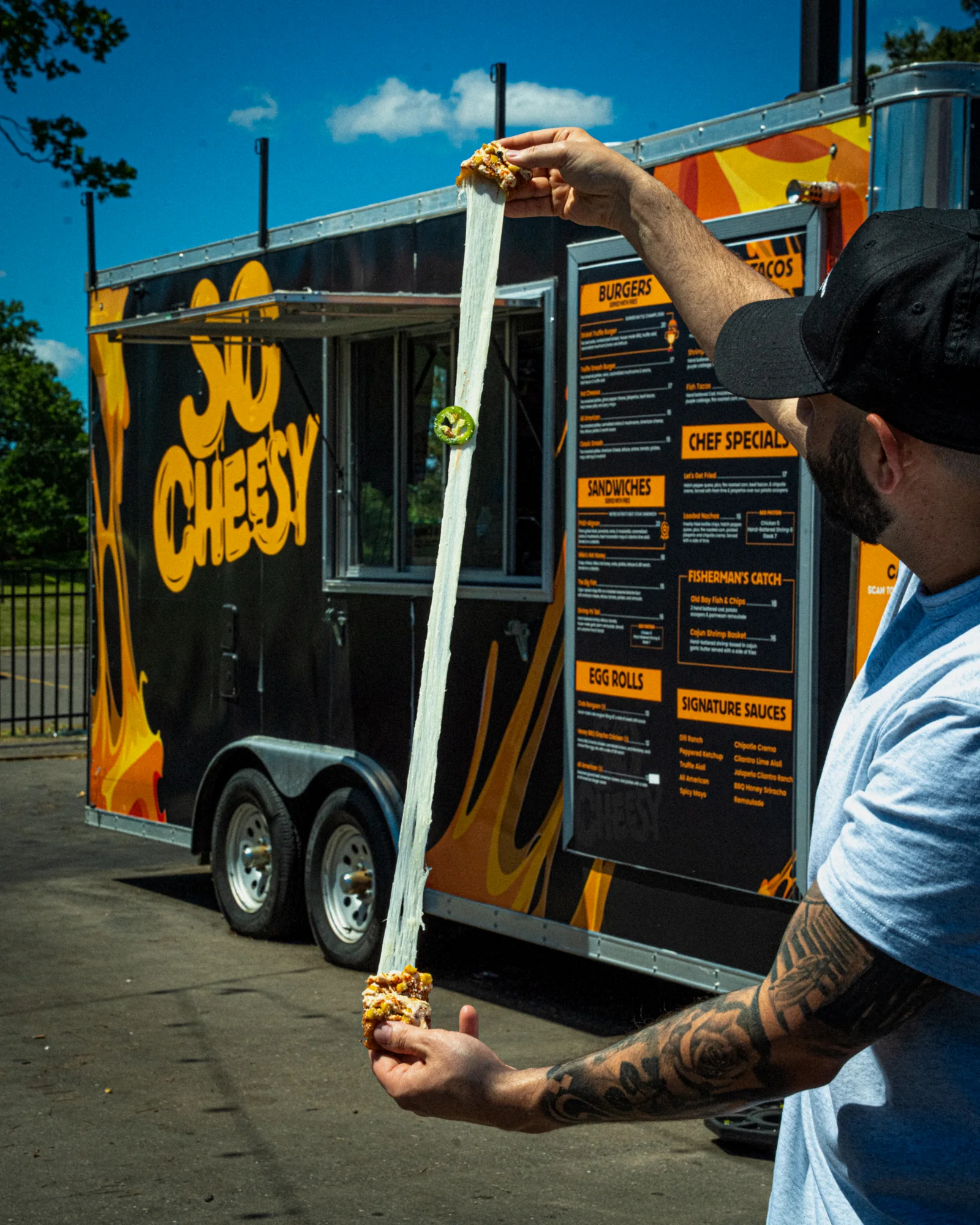 A mozzarella brick pulled apart into a cheese stretch longer than an arm, in front of the So Cheesy truck